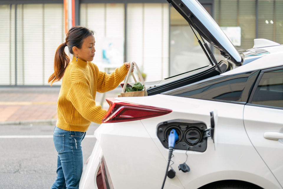 Mid adult woman loading groceries into her electric car. 