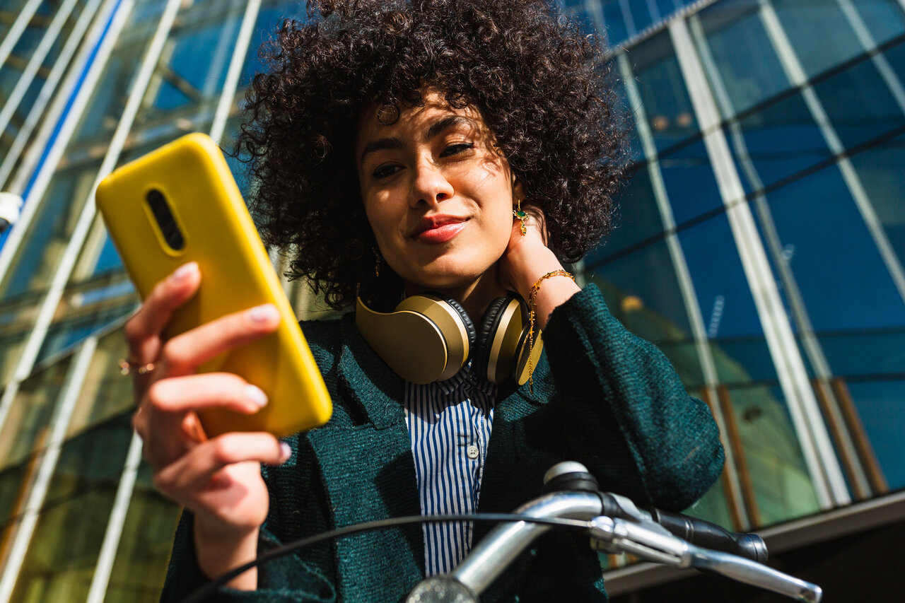 Low angle view of the portrait of a woman using a mobile sitting on a bike in the city | © Jordi Mora igual GettyImages