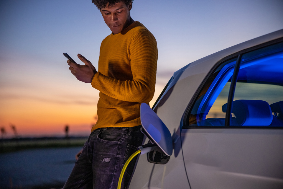 African american man using mobile phone while he is waiting for his electric car to be charged at charging station